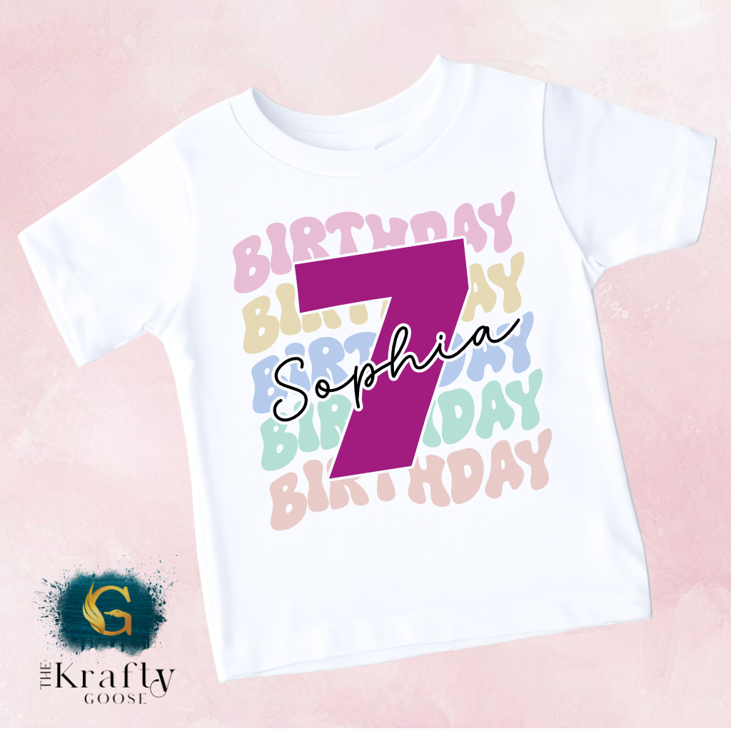 A white t-shirt with a large pink number 7 and the name "Sophia" written on it, along with colorful birthday-themed text surrounding the number.