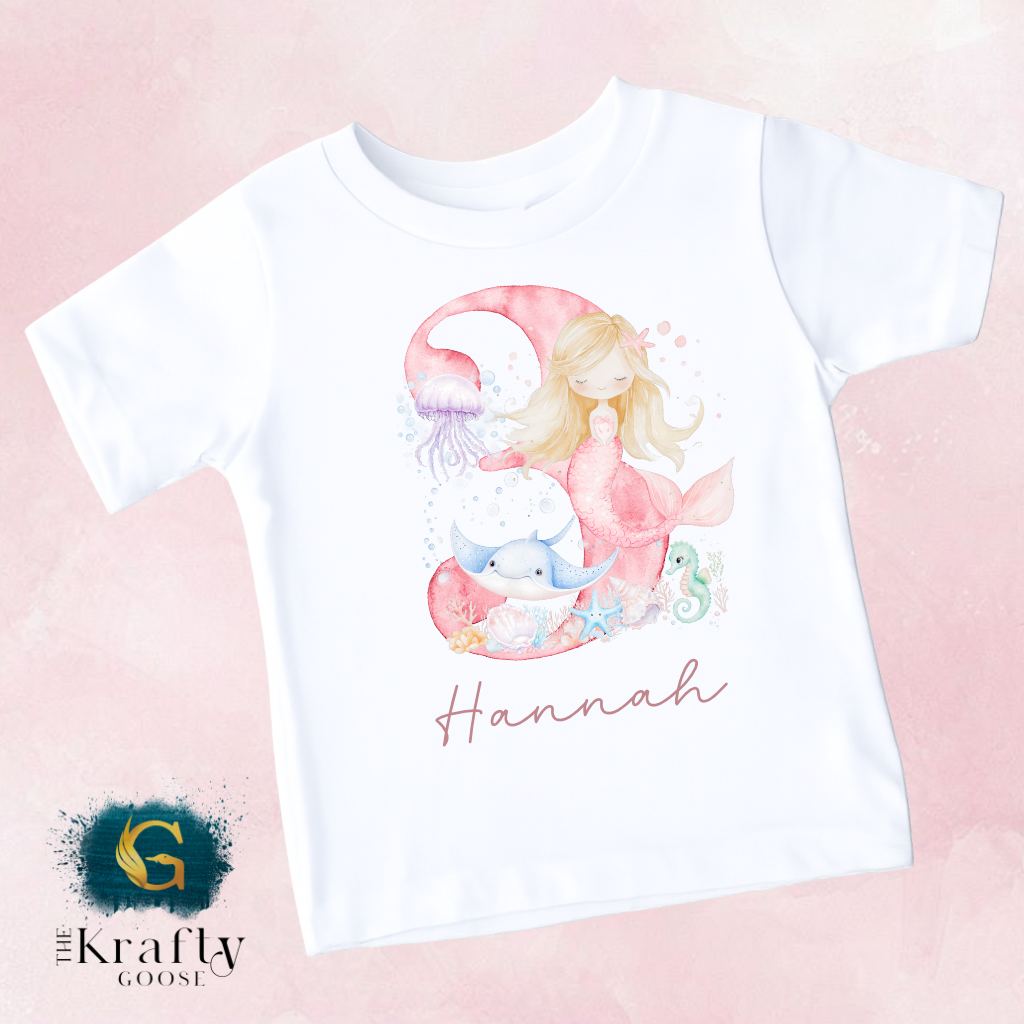 A white t-shirt with a mermaid and marine-themed design, featuring the name 'Hannah' written below the image.