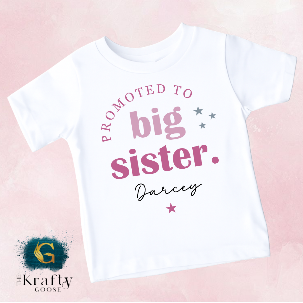 A white t-shirt with text that reads "PROMOTED TO BIG SISTER. Darcey" printed on it.