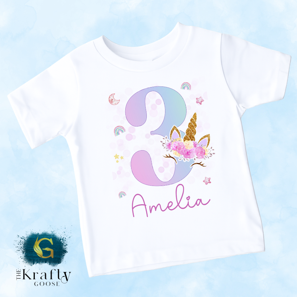 A white t-shirt with a unicorn and the number 3 printed on it, along with the name "Amelia" written below.