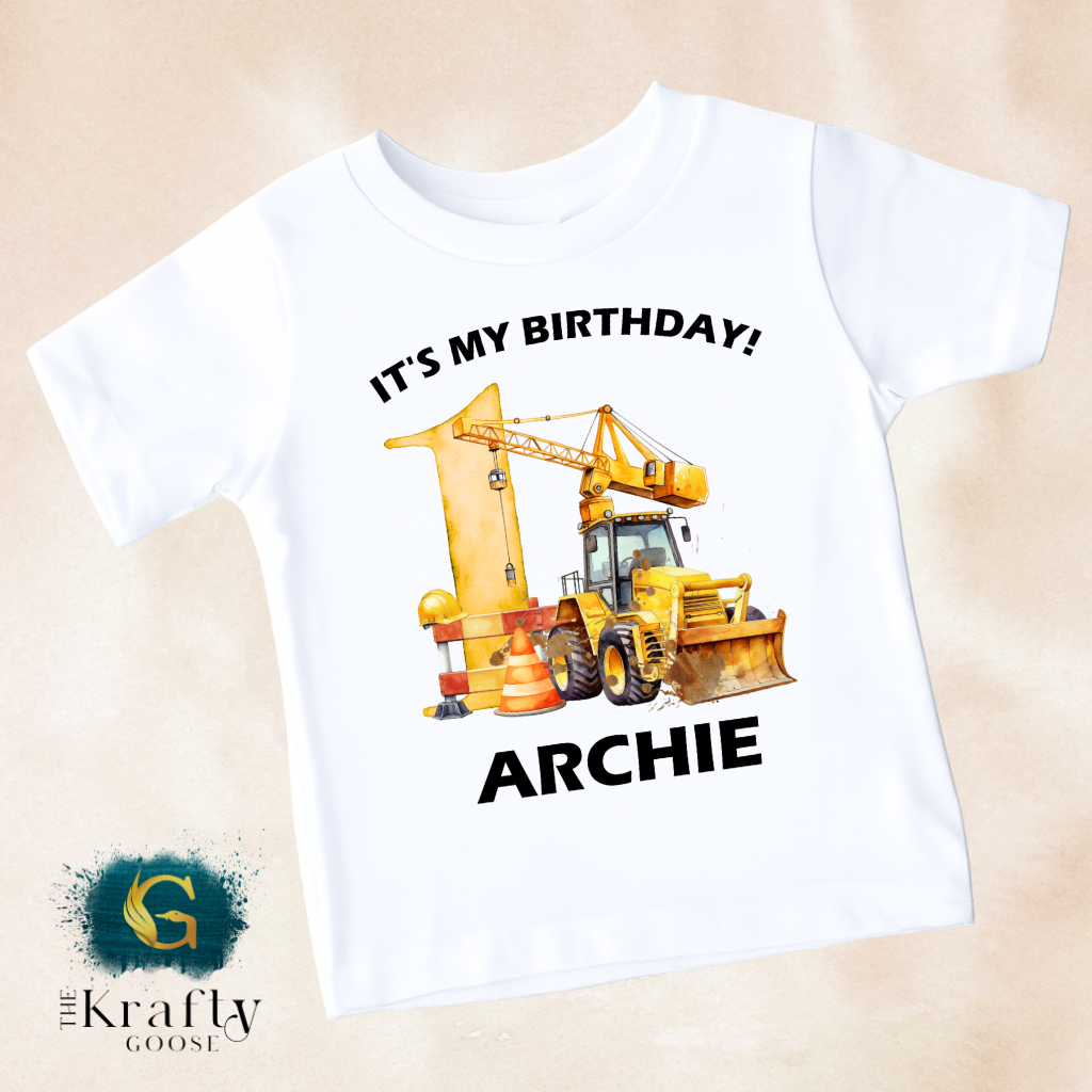 A white t-shirt with a graphic design featuring a yellow construction vehicle and the text "It's my birthday! ARCHIE" printed on it.