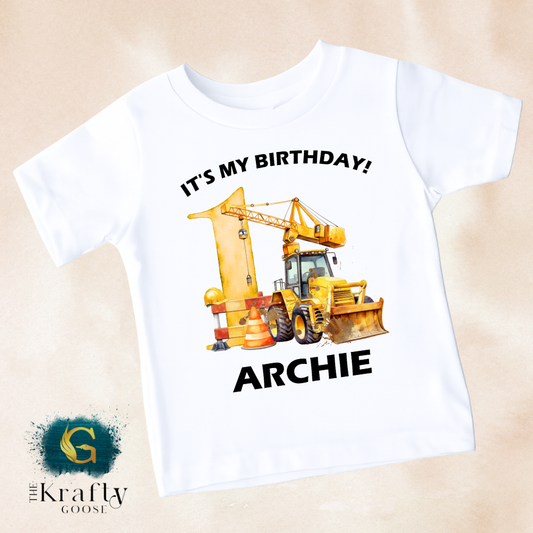 A white t-shirt with a graphic design featuring a yellow construction vehicle and the text "It's my birthday! ARCHIE" printed on it.