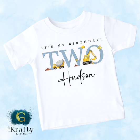 A white t-shirt with a graphic design featuring a construction vehicle and the text "It's my birthday! Two Hudson" printed on it.