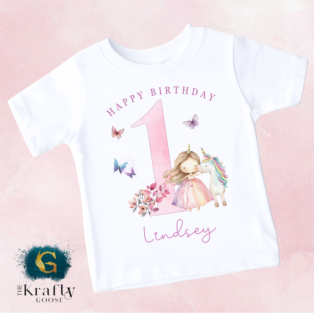 A white t-shirt with a pink number one and a unicorn, along with the text "Happy Birthday" and "Lindsey" printed on it.