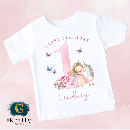 A white t-shirt with a pink number one and a unicorn, along with the text "Happy Birthday" and "Lindsey" printed on it.