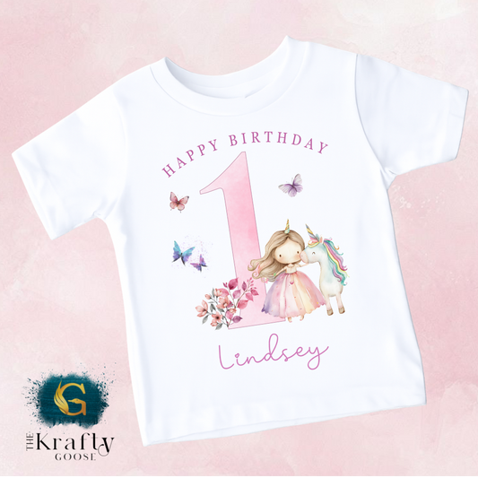 A white t-shirt with a pink number one and a unicorn, along with the text "Happy Birthday" and "Lindsey" printed on it.