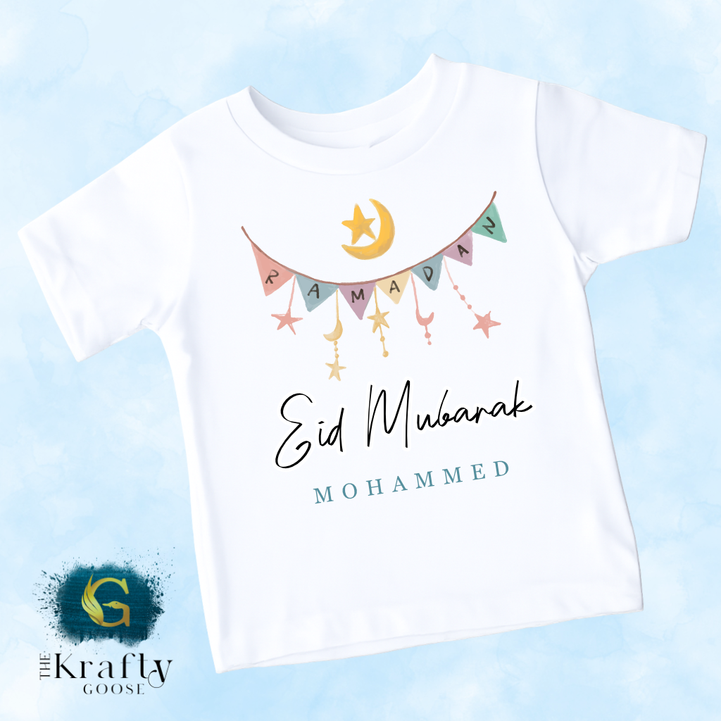 A white t-shirt with a graphic design featuring a crescent moon, stars, and the text "Eid Mubarak" and "MoHAMMED" printed on it.