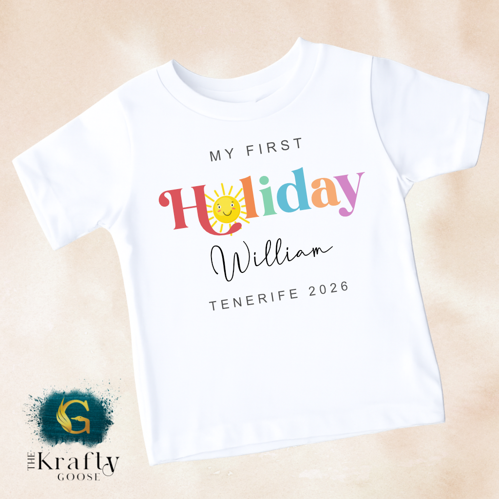 A white t-shirt with colorful text and a sun graphic, along with the text "My first Holiday William Tenerife 2026" printed on it.
