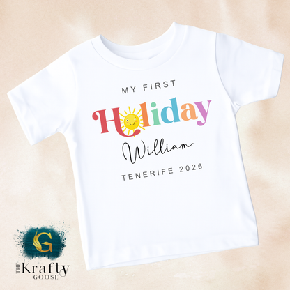 A white t-shirt with colorful text and a sun graphic, along with the text "My first Holiday William Tenerife 2026" printed on it.