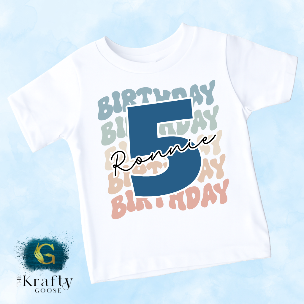 A white t-shirt with a large number 5 and the name "Ronnie" written on it, along with a colorful birthday-themed design.